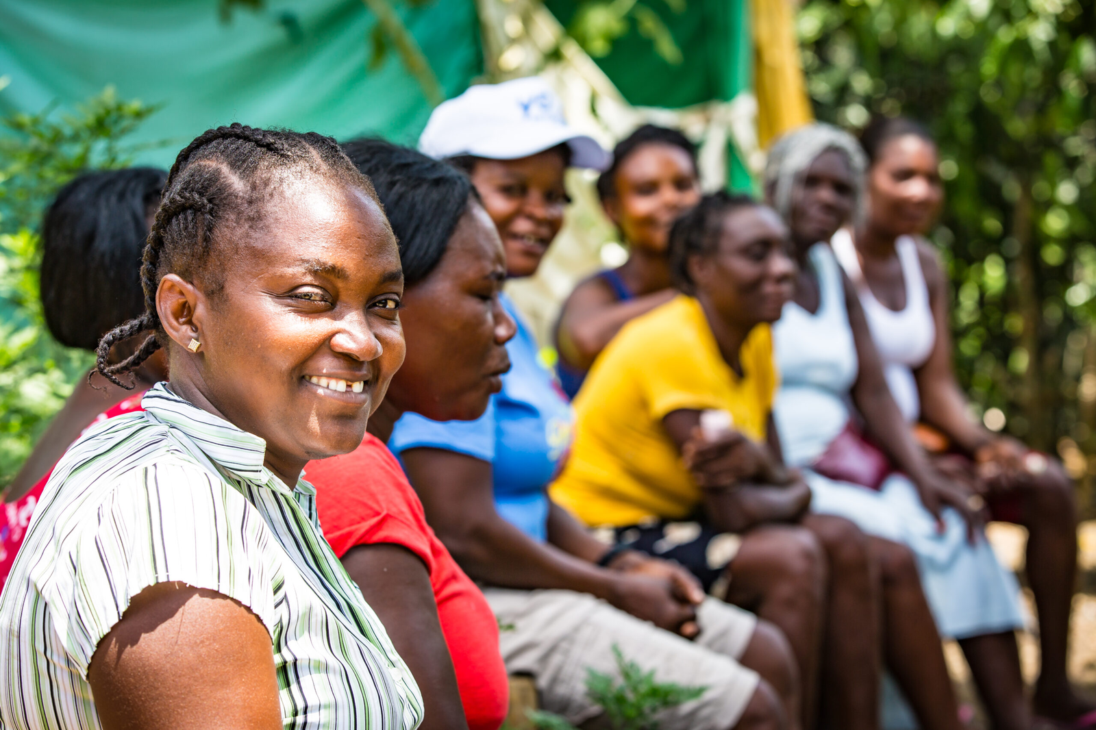 A group of smiling women and children sitting together in an outdoor setting.